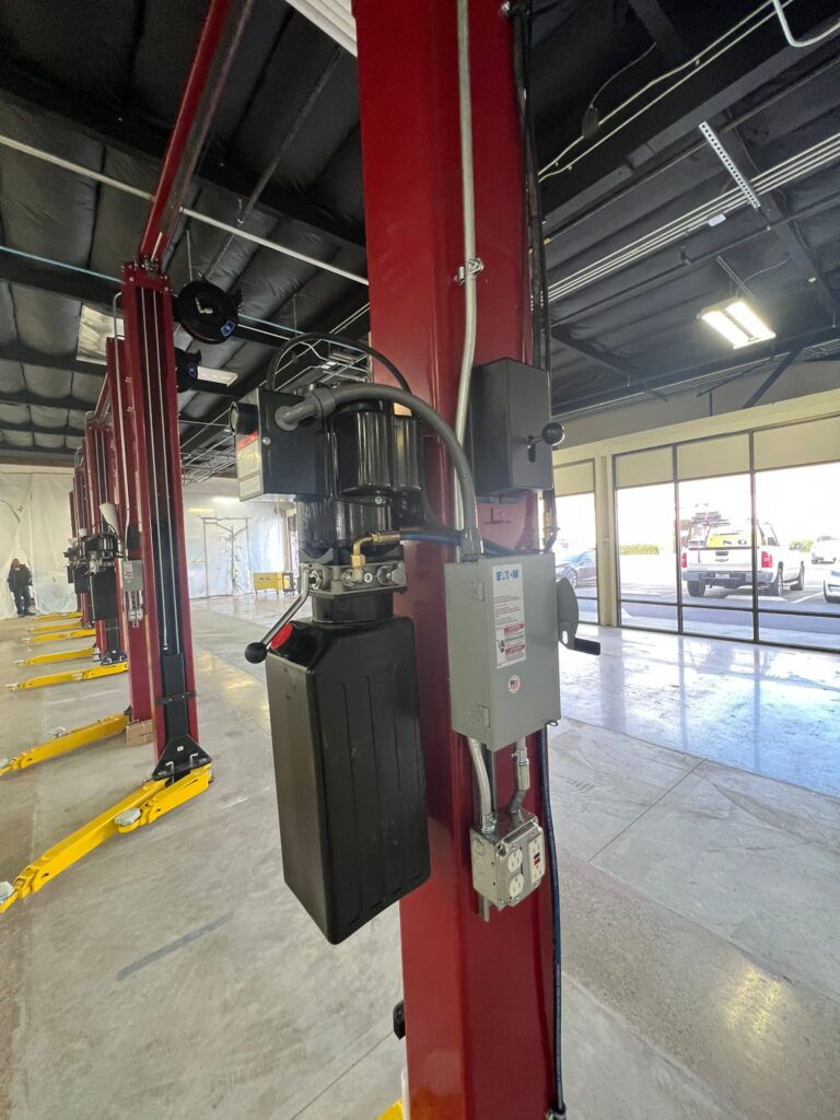 Vertical shot of overhead lighting, wiring, or conduit in the Tesla service center bay.